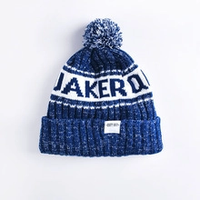 Detail of blue and white knitted pom-pom beanie featuring JAKERO text and soft texture