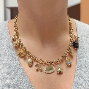 Gold charm necklace with diverse pendants like cherry and Eiffel Tower on a model