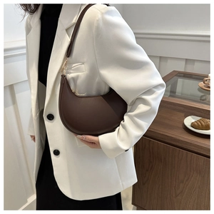 Detailed view of deep brown crescent shoulder bag on a model wearing a white blazer