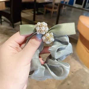 Gros plan d'un chouchou noeud vert grisâtre avec perles et strass sur tissu brillant
