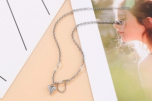 Détail du collier argenté avec maillons mixtes et pendentif cœur sur fond rose