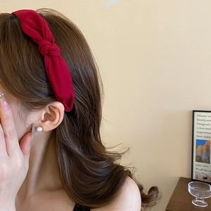 Elegant deep red fabric headband with twist knot design worn by woman on long wavy hair