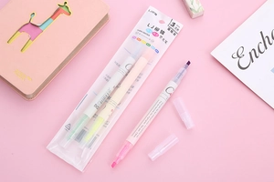 Close-up of three dual-tip colored highlighters set on pink notebook background