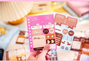 Detail of pink and blue daily calendar stickers held over a cozy journaling workspace