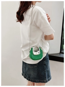 Detail of a mini green crossbody bag with a silver metal handle and chain strap