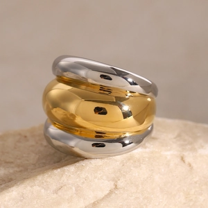 Polished two-tone chunky ribbed ring in gold and silver finish on a stone pedestal