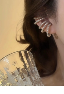 Close-up of elegant white multilayer pearl ear cuff worn on model in warm lighting