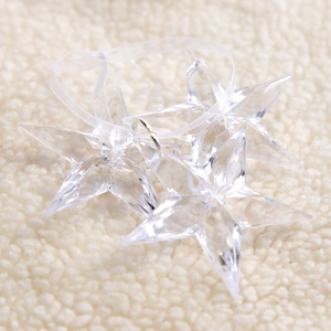 Clear 3D star snowflake ornaments hanging with ribbon on white faux fur background