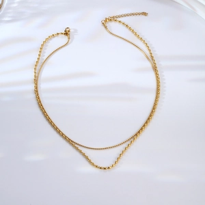 Double-layered gold titanium steel necklace with elegant seed beads on a white surface