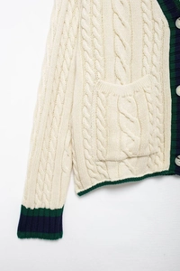 Detail of cable knit cardigan featuring contrast striped trim and white buttons on ivory fabric