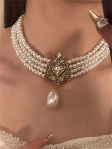 Macro detail of multi-layer pearl necklace with ornate gold pendant and teardrop pearl