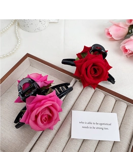 Detailed view of red and pink fabric rose flower claw clips on beige velvet surface