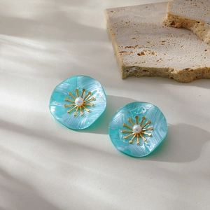 Detail of blue flower stud earrings with a pearl center and gold-plated metal accents