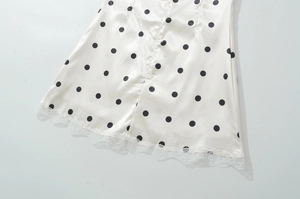 Detailed close-up of white satin fabric with black polka dots and delicate lace trim