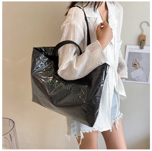 Detail of a large black glossy tote bag with text worn by a model in a casual setting