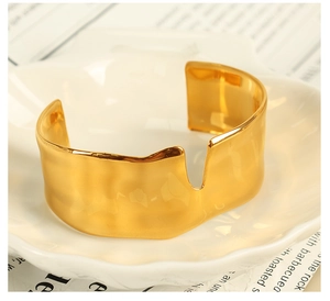 Detailed close-up of wide gold-plated open cuff bracelet on elegant white floral tray