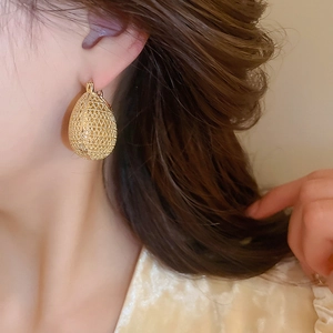 Close-up of golden teardrop earrings with intricate woven mesh texture on a model