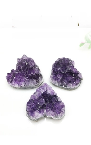 Three heart-shaped natural amethyst clusters showing deep purple crystals on white base