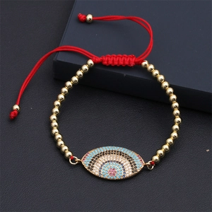 Detail of red rope bracelet with gold beads and a colorful evil eye zircon charm