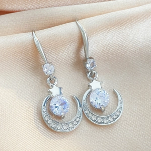 Pendientes de estrella y luna brillantes con circonitas sobre fondo de seda