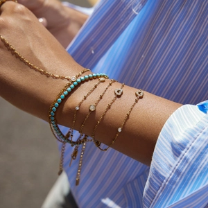 Close-up of layered gold bracelets with turquoise beads and heart charms on a wrist