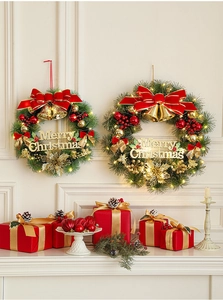 Close-up of lighted Christmas wreath with red bows and gold ornaments on a white wall