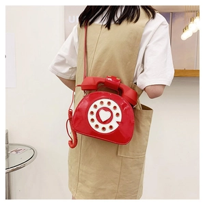 Macro detail of a red retro telephone crossbody bag featuring a glossy patent finish