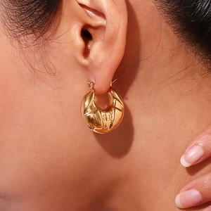 Detail of chunky gold geometric hoop earring with wavy texture worn on ear lobe