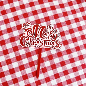 Macro shot of red acrylic Merry Christmas cake topper on red white plaid cloth