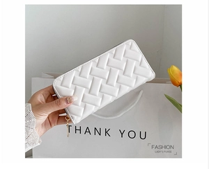 Detail of white PU leather clutch with woven texture held against a gift bag background