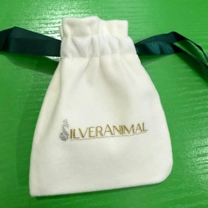 Close-up of a white velvet drawstring jewelry pouch with a green satin ribbon and silver logo