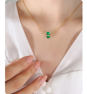 Close-up of a gold necklace featuring a green rectangular gemstone pendant on a model