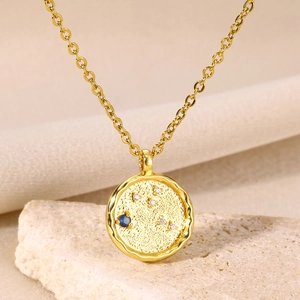 Detail shot of a hammer-textured 18K gold-plated zodiac necklace with a blue gemstone