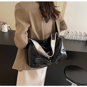Detail of black glossy Boston bag with wide silver strap and casual text label