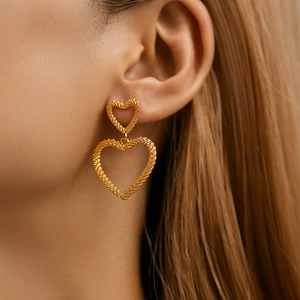 Detail of golden heart drop earrings with textured matte finish on a female model