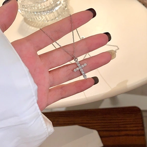 Close-up of a sparkling moissanite cross pendant necklace held in a person's hand