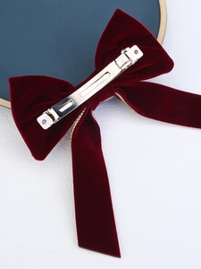 Macro view of dark red velvet bow hair clip with gold chain trim and silver metal clasp
