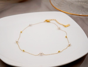 Detailed view of a gold-plated necklace with fresh water pearls on a ceramic dish