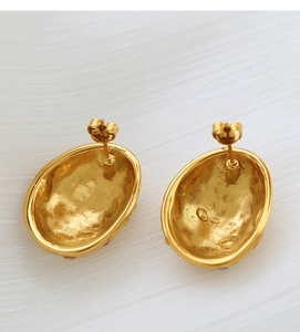 Macro view of gold oval stud earrings with hammered texture and purple crystal stones