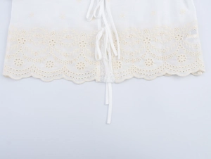 Détail du tissu blanc avec broderie florale en dentelle beige et un nœud délicat