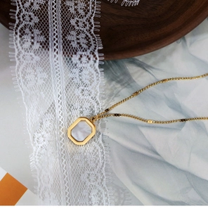 Detailed close-up of a square shell pendant on a gold necklace over lace background