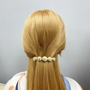 Detailed view of a golden spherical metal hair clip holding a model's half-tied hairstyle