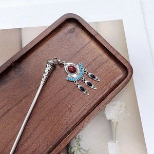 Detailed view of a vintage silver hair stick with colorful gems and tassels on wood