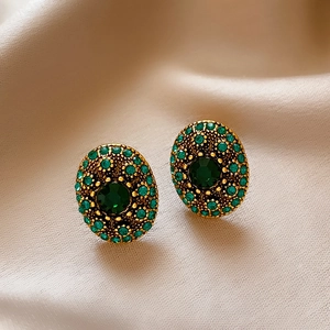 Macro detail of vintage gold oval earrings with green crystal on beige silk backdrop