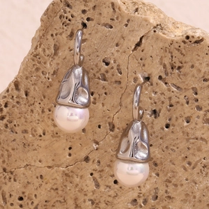 Detailed view of silver textured metallic drop earrings with white pearls on a natural rock