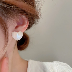 Close-up of minimalist heart stud earrings with iridescent pearlescent finish on model
