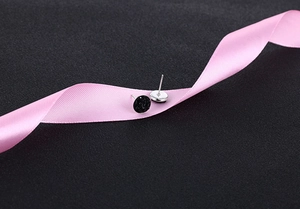 Close-up of black round crystal stud earrings on pink silk ribbon with silver pins