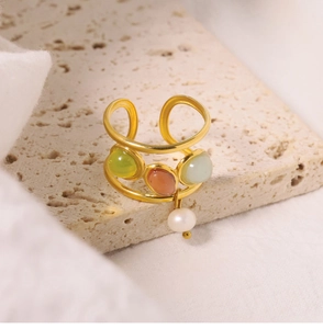 Detail of gold open ring with three colored gemstones and a white pearl pendant