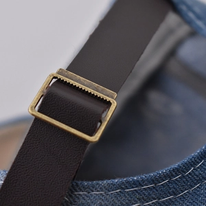 Detail of adjustable leather strap and bronze metal buckle on denim baseball cap