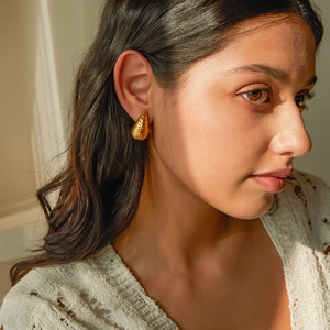 Detail of 18k gold plated stainless steel teardrop earrings with striped texture on model